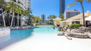 A resort pool with palm trees, a bridge, and buildings in the background.