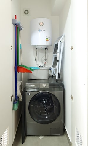 Un lavadero pequeño con un calentador de agua VOLKER, una lavadora Samsung y un tendedero.