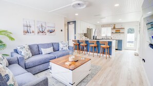 A modern living room with a blue sofa, a coffee table, and a kitchen area with a bar.