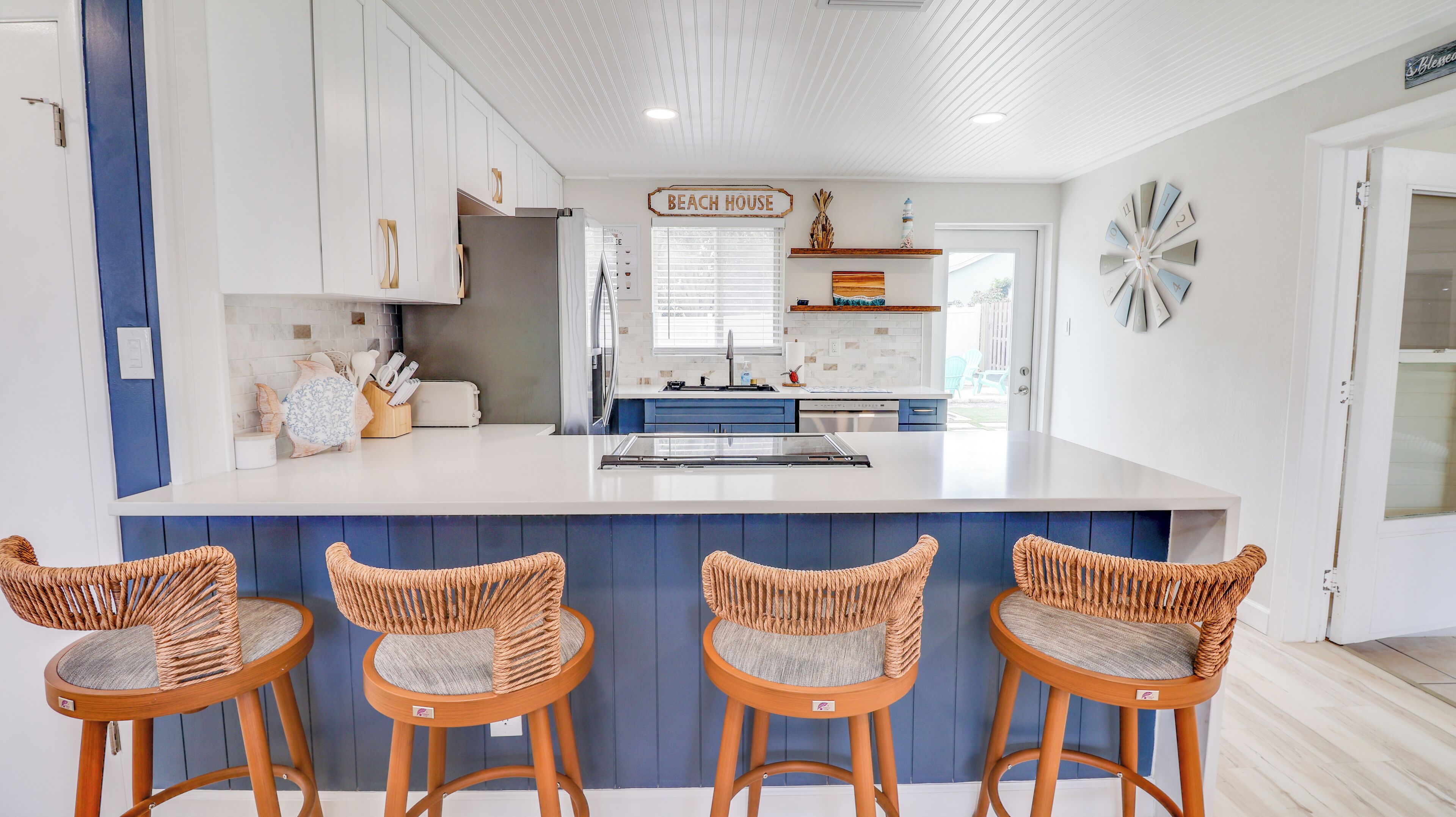 A modern kitchen with a central island, blue cabinets, and wicker chairs.