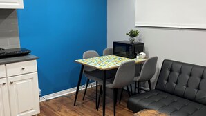 A compact living space with a dining table, two chairs, a black sofa, a small kitchen area with a microwave, and a white cabinet. - Private apartment(bedroom, living, kitchen, bath) (Pincourt)