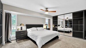 Ein modernes Schlafzimmer mit einem großen Bett, einem Deckenventilator und einer Schiebetür zum Kleiderschrank.