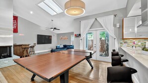 Ein modernes Wohnzimmer mit Tischtennisplatte, Kamin, einer Couch und einem großen Fenster mit Vorhängen.