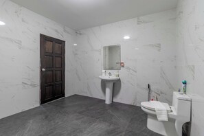 A bathroom with a marble wall, a dark floor, a white sink, and a toilet.