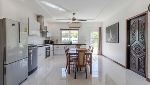 Une cuisine moderne avec des meubles blancs, des appareils en acier inoxydable et un coin repas comprenant une table et des chaises en bois.