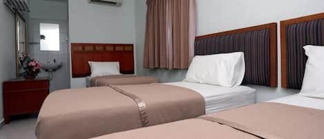 Ein Hotelzimmer mit drei Einzelbetten, einem Holz-Kopfteil, einem Schminktisch und einem Spiegel.