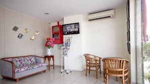 A room with a sofa, chairs, a TV, a vase with flowers, and a bulletin board. - Hotel Rembia (Sungei Petai)
