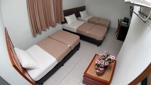 A room with three beds, a wooden nightstand, a small table with flowers, and a wall-mounted towel rack. - Hotel Rembia (Sungei Petai)