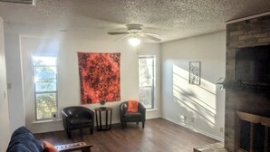 A living room with a fireplace, two leather chairs, a coffee table, and a tapestry on the wall. - Game Day Getaway 1 | Walk to OSU | Prime Location (STILLWATER)