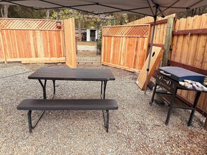 Ein Terrassenbereich im Freien mit Tisch und Bänken, umgeben von Holzzaun und einer Überdachung.