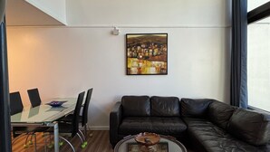 En moderne stue med et glasbord, sort lædersofa og et billede på væggen.