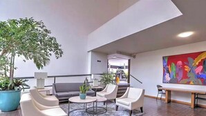 En moderne lobby med en grå sofa, hvide lænestole, et sofabord og en stor stueplante.