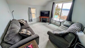 A living room with two sofas, a TV, and a window with a view. - The Founder's Vista Suite Spacious, Panoramic Ocean Views (Alert Bay)