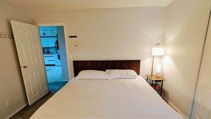 A hotel room with a large bed, a bedside table with a lamp, and a door leading to a kitchenette. - The Founder's Vista Suite Spacious, Panoramic Ocean Views (Alert Bay)