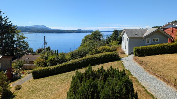 A residential area with a house, a gravel path, and a view of a lake with mountains in the distance. - The Founder's Vista Suite Spacious, Panoramic Ocean Views (Alert Bay)