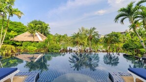 A infinity pool with lounge chairs, surrounded by lush greenery and palm trees.