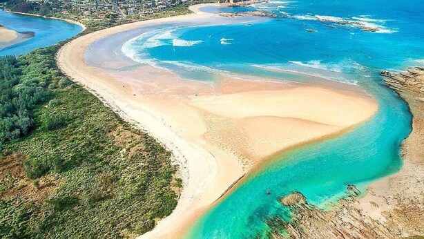 An aerial view of a coastal area with a curved sandy beach, clear turquoise waters, and a distant town. - A Classic Beach House - Waterfront Access and Short Walk to Beach (Mossy Point)