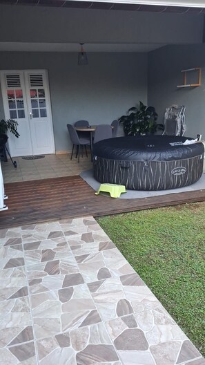 A patio area with a stone floor, a round black outdoor seating area, a dining table with chairs, and a potted plant.