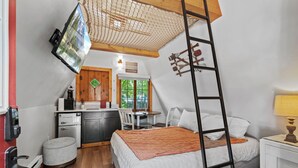 A compact room with a bed, a small kitchenette, a dining area, and a window with a view of greenery. - Timber Lodge Cabins 22 (Colorado Springs)