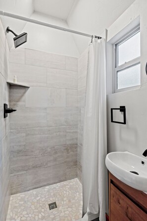 A shower with a rain showerhead, a white shower curtain, and a pebble-patterned floor. - Timber Lodge Cabins 22 (Colorado Springs)