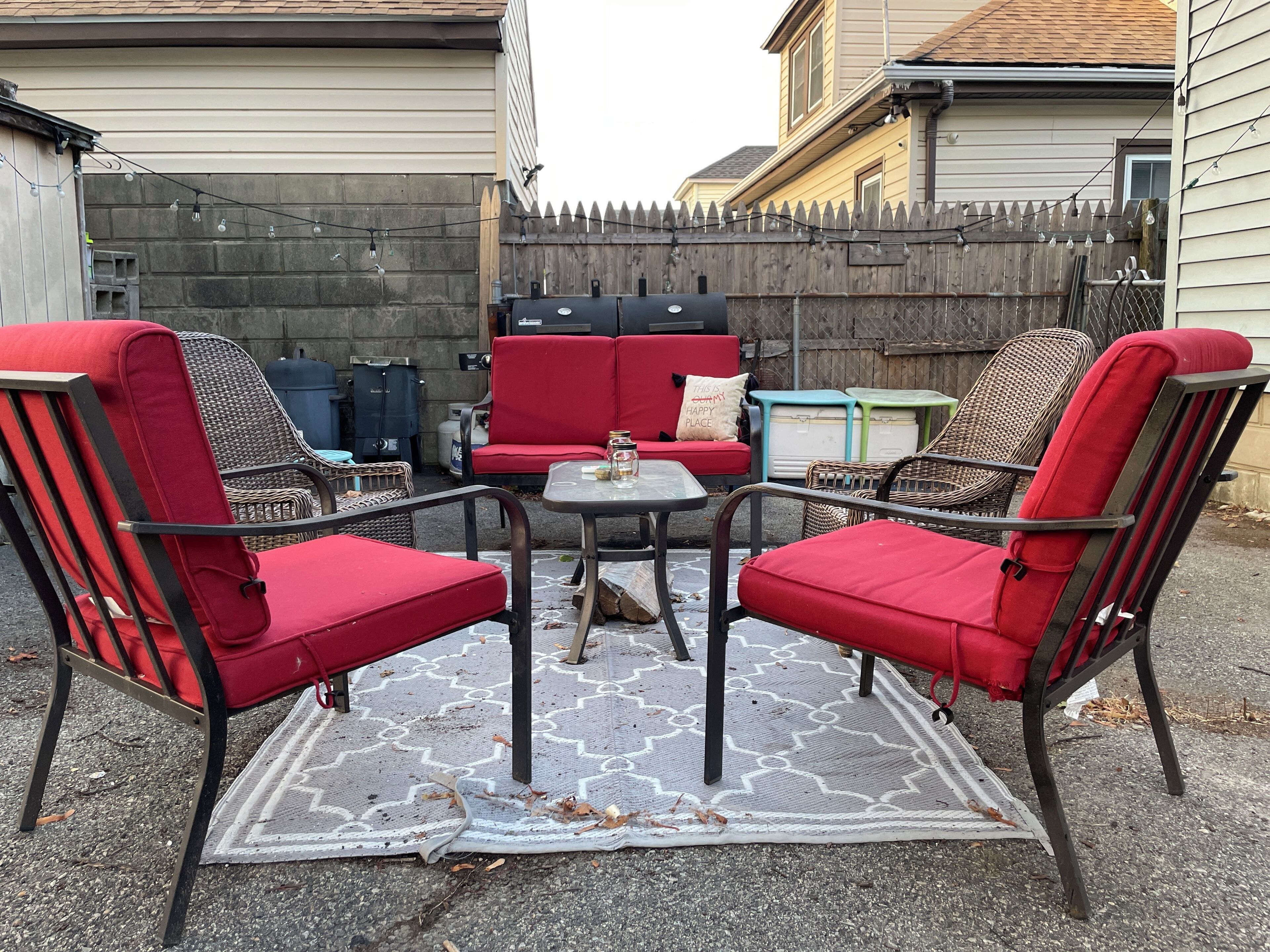 A patio with red chairs and a small table, a wooden fence, and a house in the background.