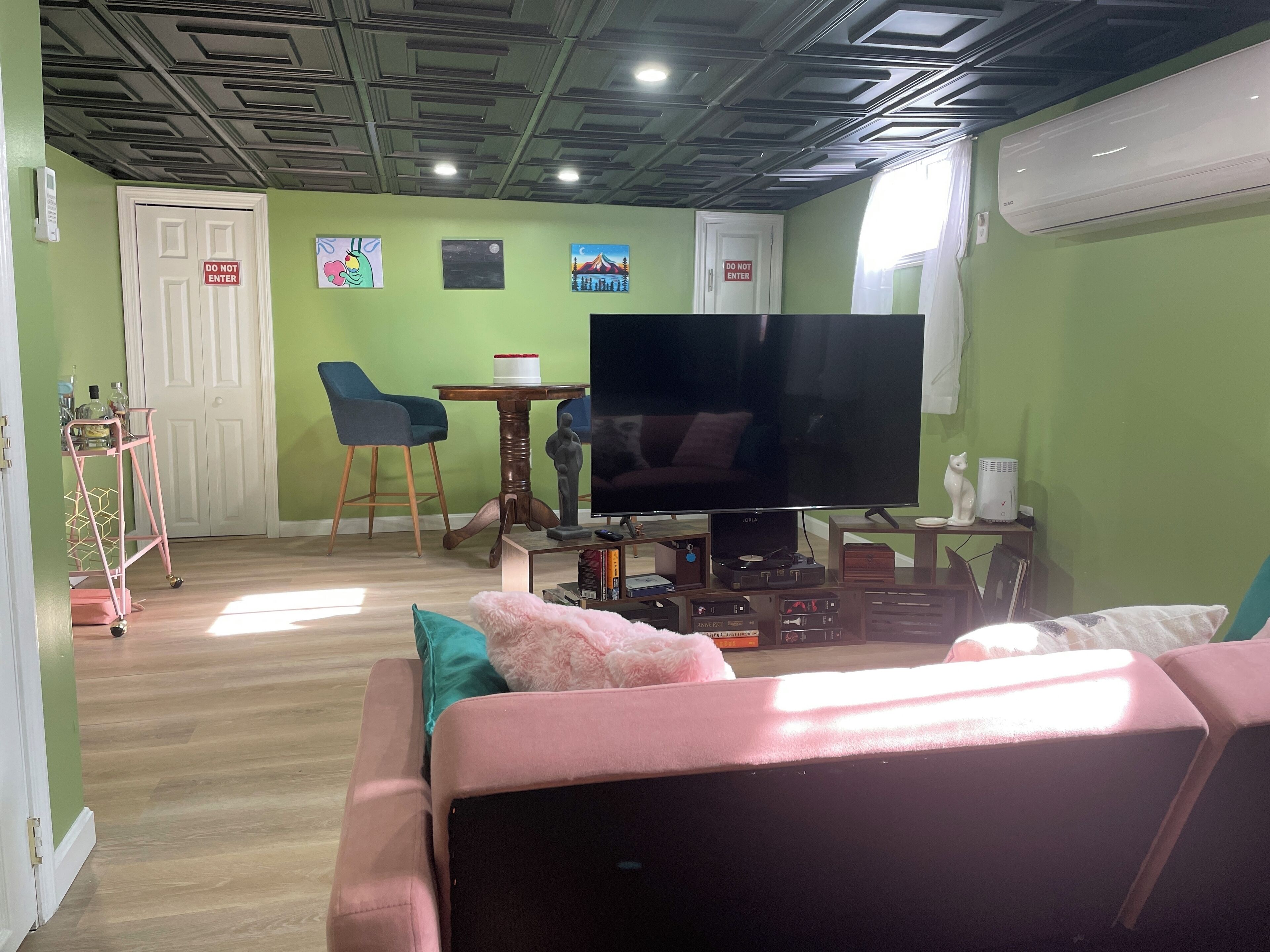 Un salon avec une télévision, un canapé et une petite table avec une chaise. Il y a deux portes, dont l’une porte l’inscription « Défense d’entrer ».