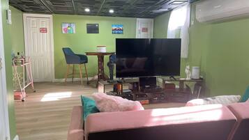 Un salon avec une télévision, un canapé et une petite table avec une chaise. Il y a deux portes, dont l’une porte l’inscription « Défense d’entrer ».