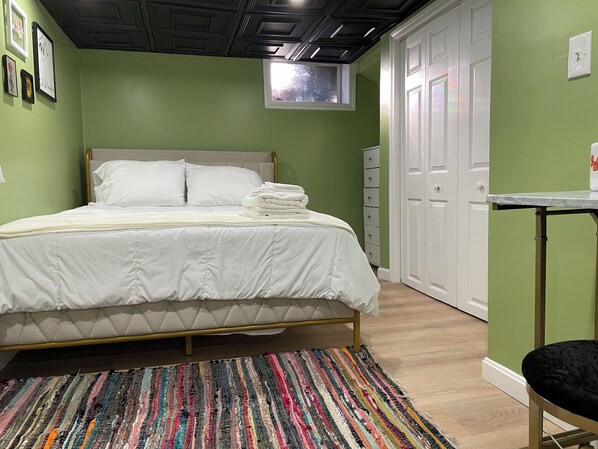 Un lit bien fait, avec une literie blanche, un tapis rayé aux couleurs vives et une petite fenêtre au-dessus du lit.
