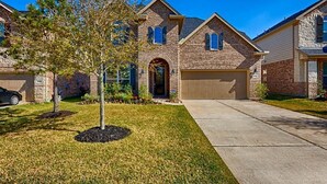 A two-story brick house with a garage, a front yard with a small tree, and a clear blue sky. - Spacious 5-bedroom Modern Stay Near - IAH-AIRPORT (Humble)