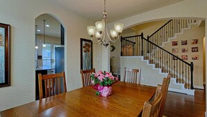 A dining area with a wooden table, chairs, a chandelier, and a staircase with a railing. - Spacious 5-bedroom Modern Stay Near - IAH-AIRPORT (Humble)
