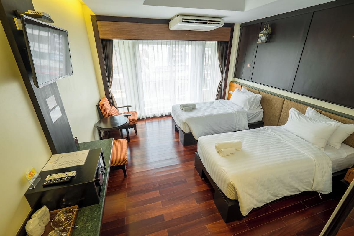 A hotel room with two beds, a desk with a computer, a TV, and a window with curtains.