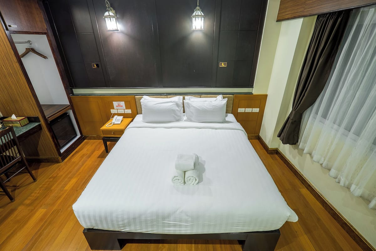 A neatly made bed with white linens and a towel centerpiece, a wooden nightstand with a phone, a wooden chair, and a small table with a tissue box.
