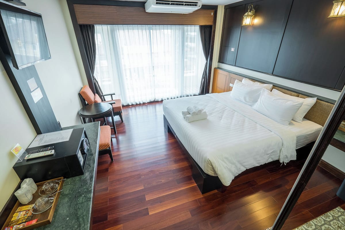 A hotel room with a large bed, a desk with a computer, a chair, and a small table with a tray of snacks.