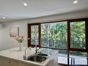 A kitchen with a double sink, a vase with flowers, and a view of a balcony with trees.