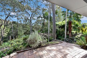 A patio with a brick floor, surrounded by various plants and trees.