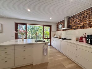 A modern kitchen with white cabinetry, a central island, a brick accent wall, and a window with a view of greenery.