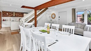 Une cuisine moderne avec un mur de briques en guise de pare-feu, un coin repas avec des meubles blancs et un escalier menant à un niveau supérieur.