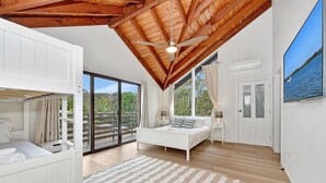 Une chambre avec un lit superposé, un lit simple, un ventilateur de plafond, une grande fenêtre et une vue sur l’extérieur.