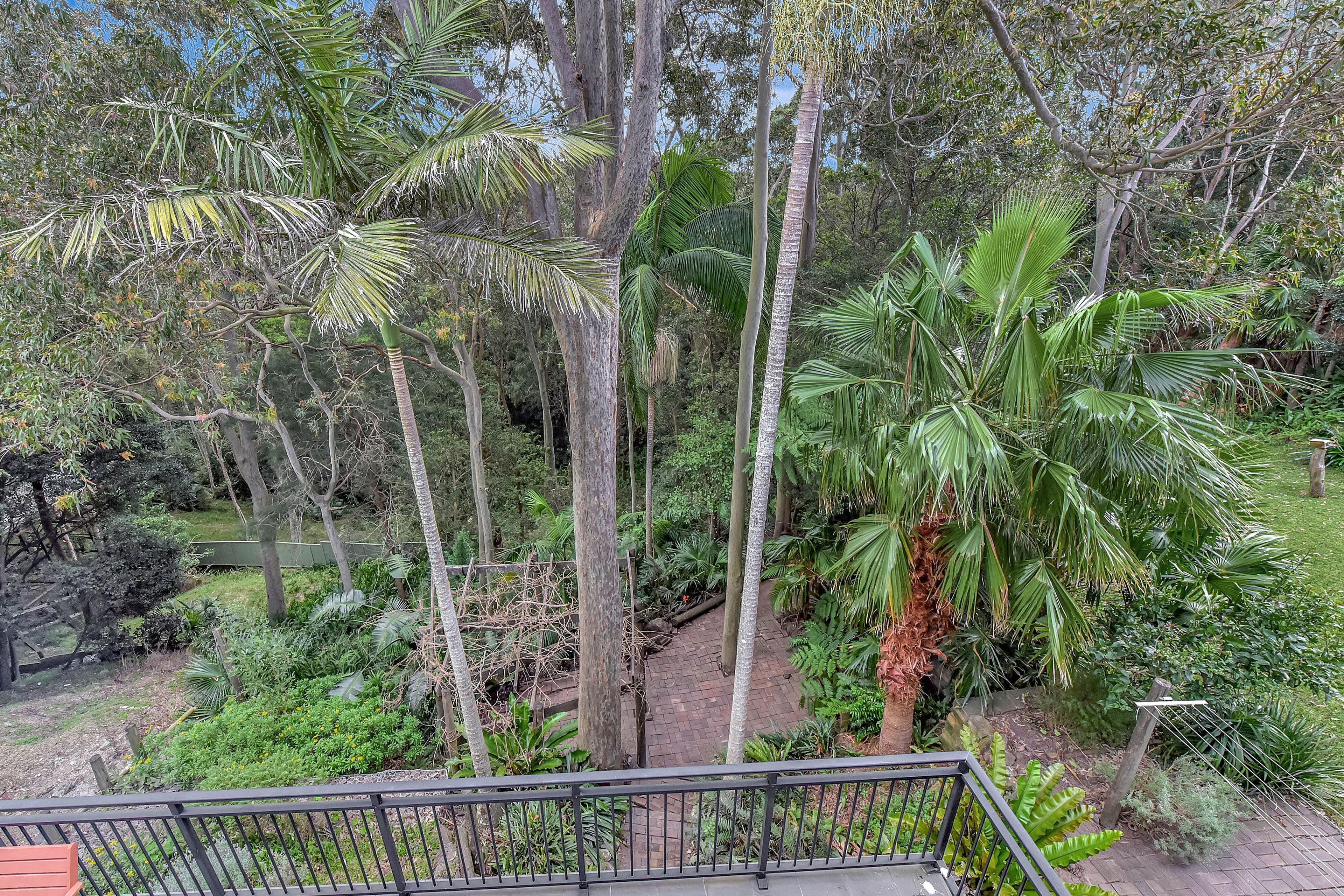A balcony with a view of a lush garden with various trees and plants.