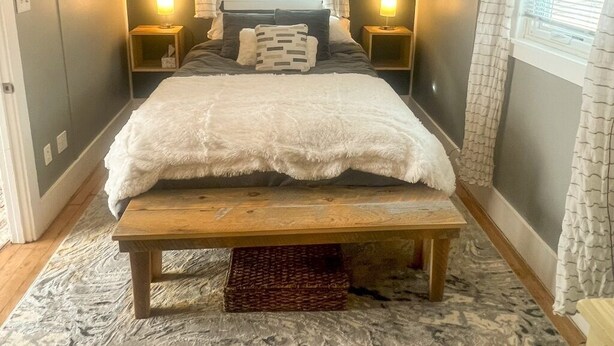 A bedroom with a large bed, bedside lamps, a wooden bench, and a window with curtains.