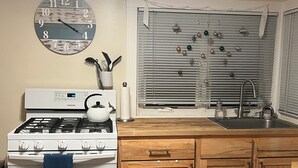A kitchen with a stove, sink, wooden cabinets, a clock, and decorative ornaments on the window.