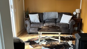 A living room with a brown leather sofa, a wooden coffee table, a cowhide rug, a fireplace, and a window with blinds.