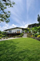 Una casa moderna con un porche cubierto, un césped cuidado y varias macetas con plantas.