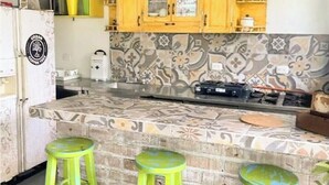 Une cuisine avec des meubles de couleur jaune, un pare-feu décoré et trois tabourets verts.