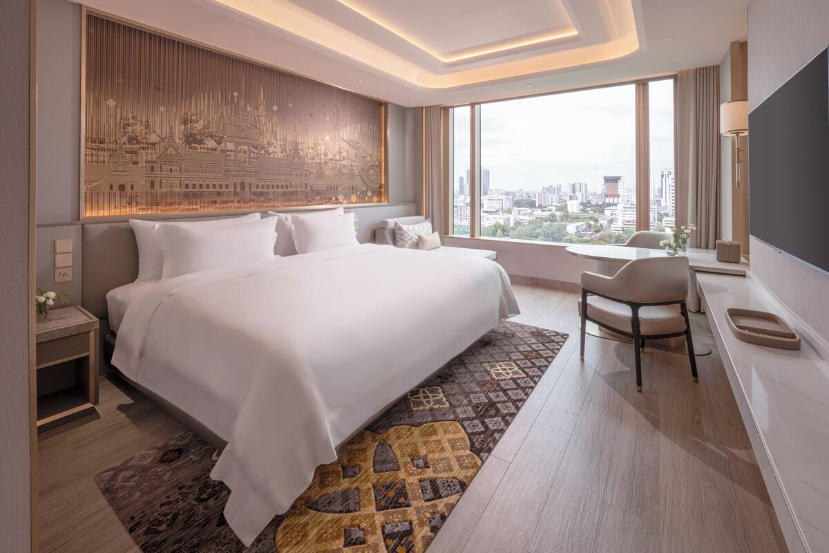 A modern hotel room with a large bed, a desk, and a city view.