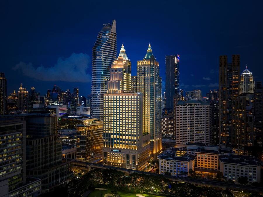 Une vue nocturne d’une ville, avec des gratte-ciel illuminés, dont un bâtiment au design distinctif, caractérisé par une forme incurvée, et un autre bâtiment dont le sommet est pointu.