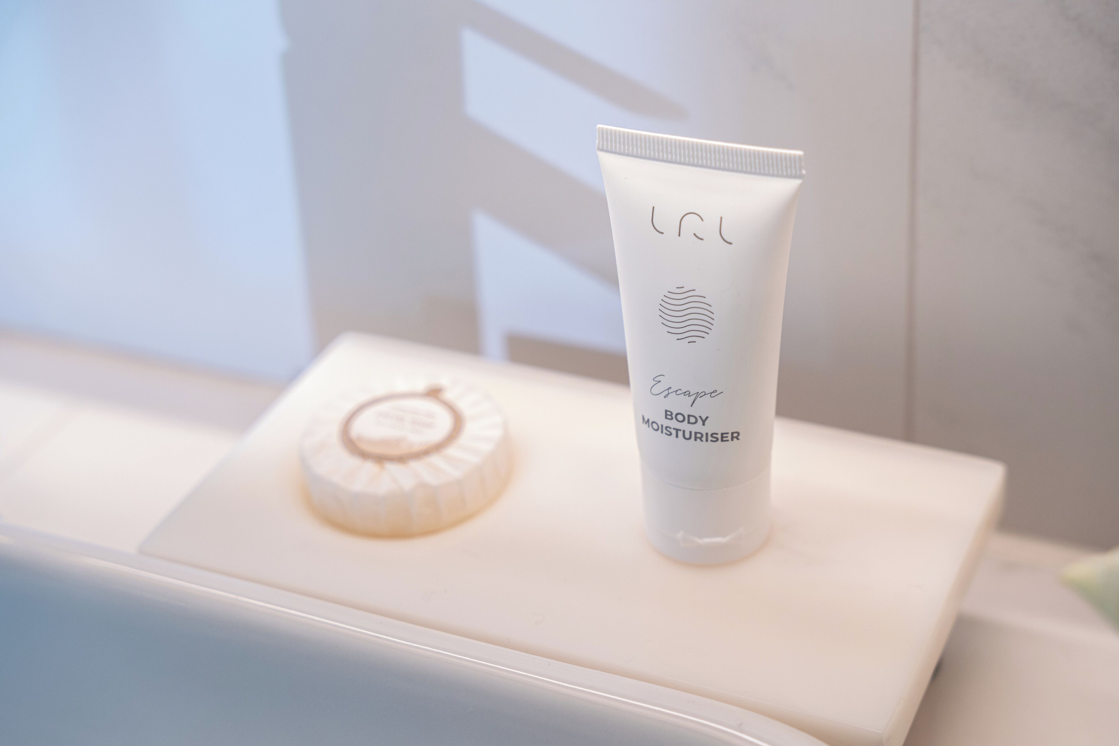 Un baño con una bañera blanca, una toalla blanca y un tubo de crema hidratante sobre una superficie blanca.