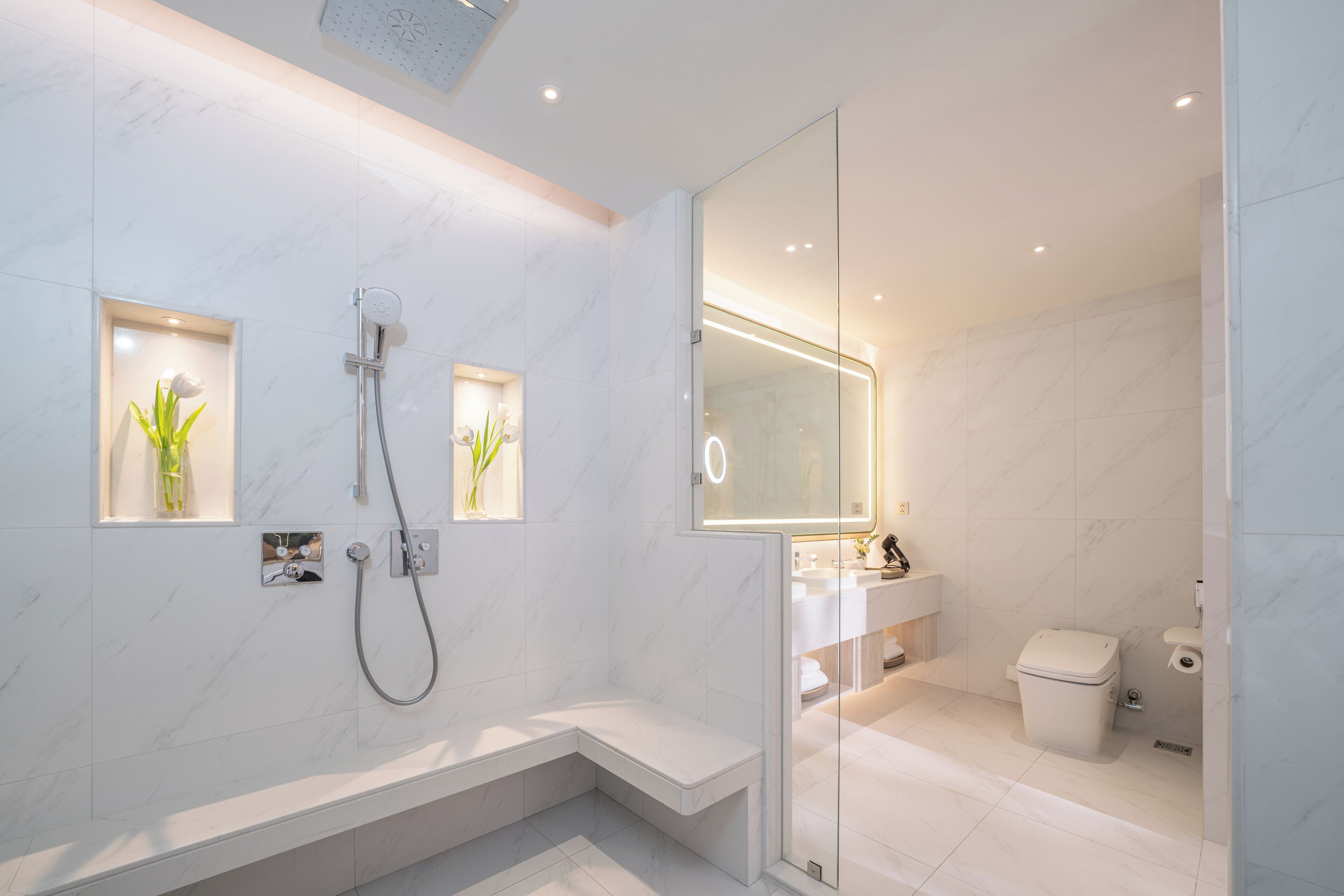 A modern bathroom with a glass-enclosed shower, marble walls, and a built-in bench.