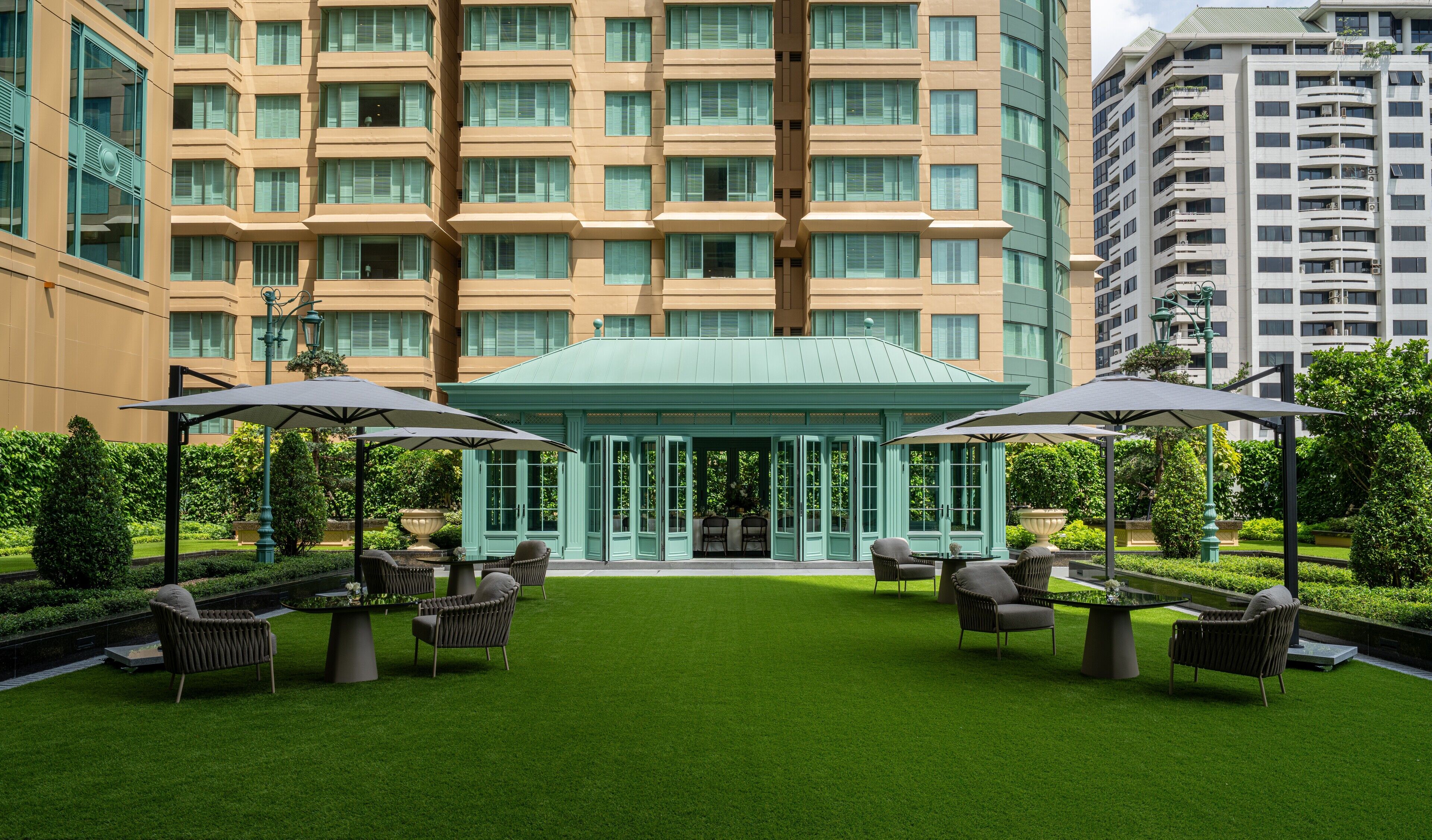 A hotel courtyard with a green lawn, outdoor seating, and a building with multiple floors and balconies.