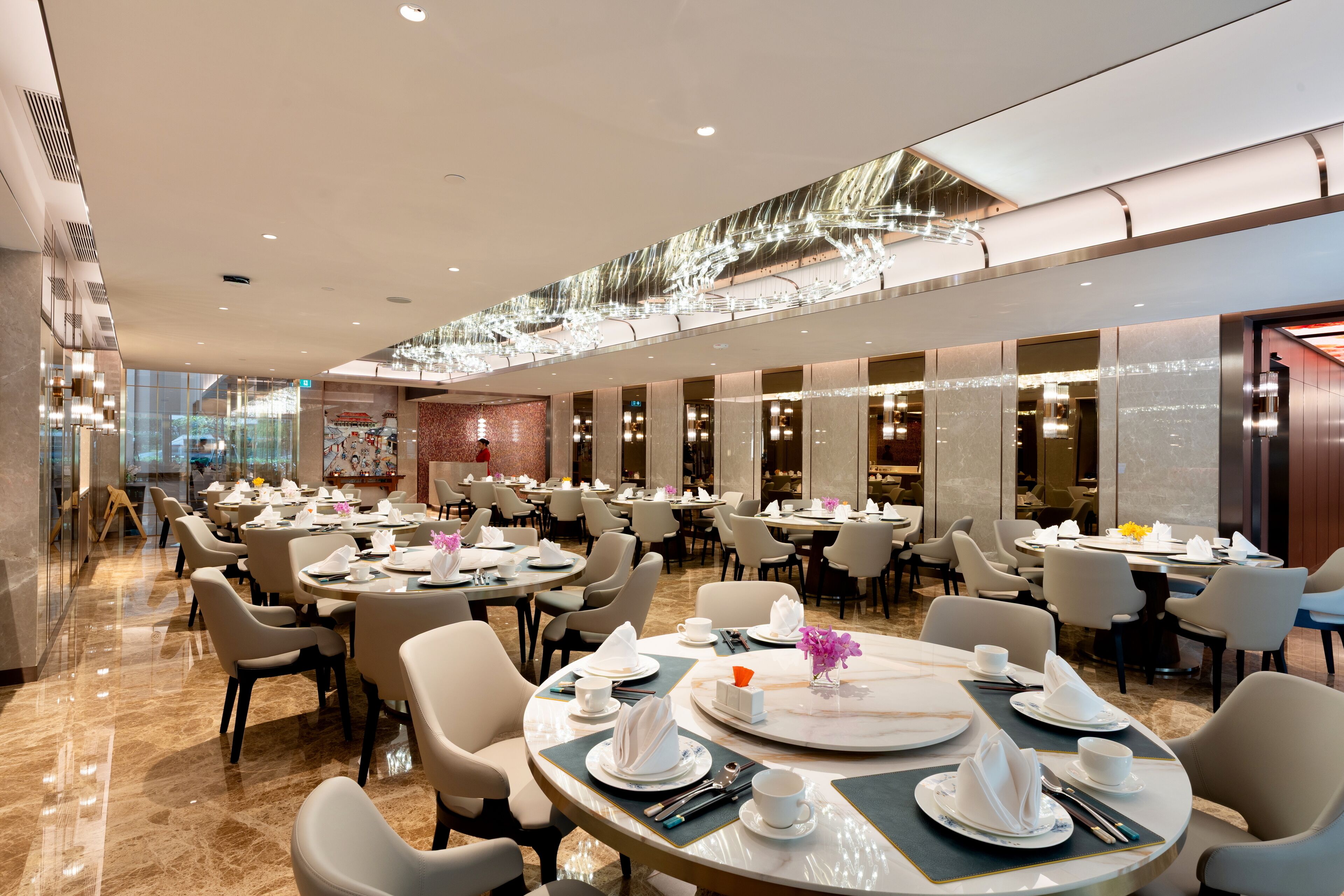 A spacious dining area with multiple round tables, each set with white tableware and chairs.